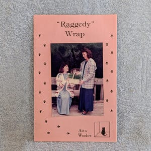 May include: A pink brochure titled "Raggedy Wrap" with a photo of two people. The brochure has paw prints around the photo and the Attic Window logo. The photo shows two people, one holding a basket.