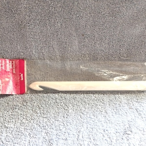 May include: A white Susan Bates Luxite plastic crochet hook in its original clear plastic packaging with a red header card. The packaging displays the text Susan Bates, Plastic Crochet Hook, 16mm, 0 US, and Luxite in white and black lettering.