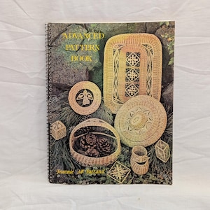 May include: A spiral-bound book titled "ADVANCED PATTERN BOOK" featuring images of woven baskets and decorative items. The cover showcases various basketry designs, including a rectangular rug, round mats, and a basket filled with pinecones. The author's name, Jeannie McFarland, is also visible.