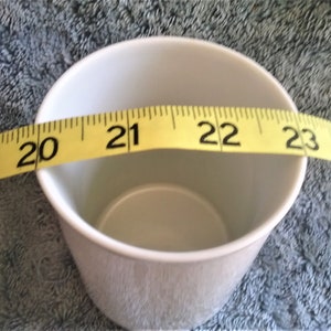 K&ouml;nnte beinhalten: Eine wei&szlig;e Keramiktasse mit einem gelben Ma&szlig;band um den Rand. Das Band misst 20 bis 23 Zoll.