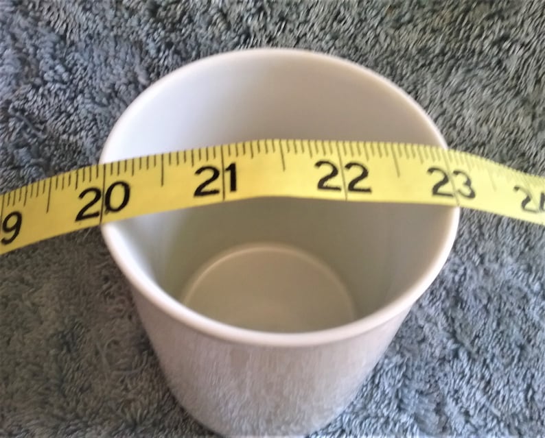 K&ouml;nnte beinhalten: Eine wei&szlig;e Keramiktasse mit einem gelben Ma&szlig;band um den Rand. Das Band misst 20 bis 23 Zoll.
