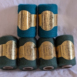 May include: Six spools of green and teal yarn with gold labels that read "Pretty Fancy" and "100th Anniversary". The labels also include the text "Sanford, FL 32771" and "Embroidery".