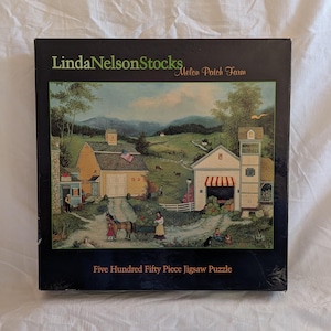 May include: A boxed jigsaw puzzle featuring a rural landscape with buildings, people, and a horse-drawn cart. The box reads "Linda Nelson Stocks Melon Patch Farm" and "Five Hundred Fifty Piece Jigsaw Puzzle". The artwork depicts a farm scene with a white building with a red awning.