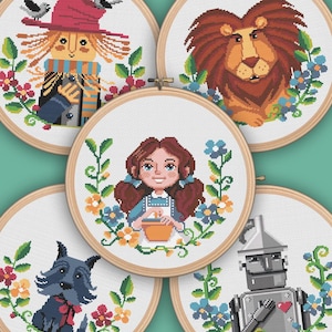 May include: Five embroidery hoop art pieces featuring characters from the Wizard of Oz. The characters are Dorothy, the Scarecrow, the Tin Man, the Cowardly Lion, and Toto the dog. Each character is surrounded by flowers and greenery.
