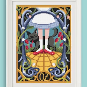 Könnte beinhalten: Ein Kreuzstichmuster mit Dorothy aus dem Zauberer von Oz, die mit ihrem Hund Toto auf dem gelben Ziegelsteinweg steht. Das Muster ist in einem goldenen Rahmen gerahmt und enthält das Wort "Oz" am unteren Rand.