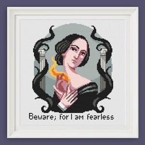 Op de afbeelding: Een kruissteekpatroon met een vrouw met donker haar en een vurig hart, omringd door een donker, wervelend ontwerp. De tekst "Beware; for I am fearless" staat onder de afbeelding.