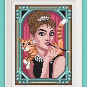 May include: A framed pixel art illustration of a woman with a cat. The woman is wearing a black dress, a pearl necklace, and a tiara. She is holding a cigarette in her hand. The cat is orange and white and is sitting on her shoulder. The frame is brown with a gold trim.
