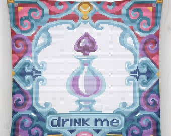 Puede incluir: Una almohada decorativa con un diseño floral azul, rosa y morado. La almohada presenta una botella de vidrio con un líquido morado y un tapón en forma de corazón. El texto "DRINK ME" está impreso debajo de la botella.