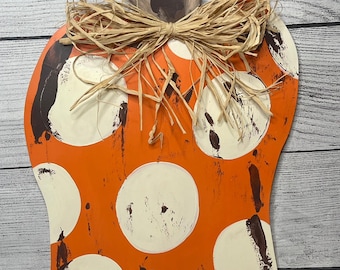 May include: Orange and white polka dot pumpkin door hanger with a brown wooden stem and a raffia bow.