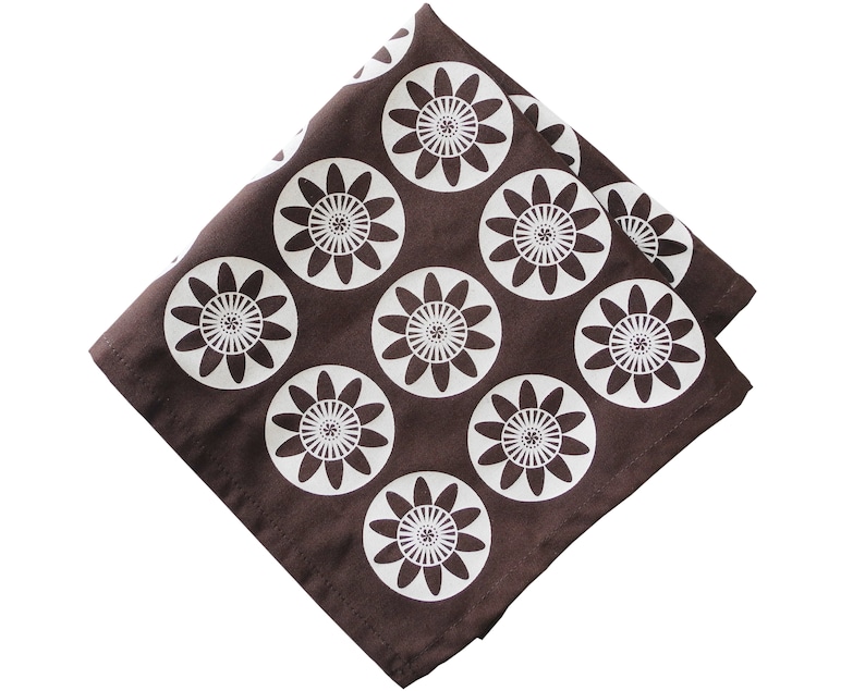 May include: A brown fabric napkin with a white floral pattern. The flowers are stylized and have a circular shape.