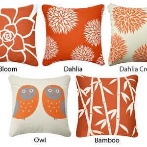 May include: Five different decorative throw pillow designs with orange and white patterns. The designs include a large orange flower, a white flower on an orange background, a white flower on a cream background, two orange owls on a cream background, and bamboo stalks on an orange background. The pillows are labeled "Bloom", "Dahlia", "Dahlia Cream", "Owl", and "Bamboo".
