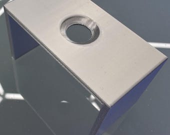 May include: A light gray, rectangular bracket with a circular hole. The bracket has a U-shaped design with a flat top and two perpendicular sides. The object is made of a solid material and has a matte finish.