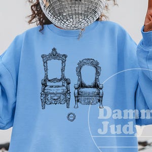 May include: A white ceramic mug with a black handle and the text "But First, Coffee" in a bold, black font. The mug is set against a neutral background, highlighting its simple design.