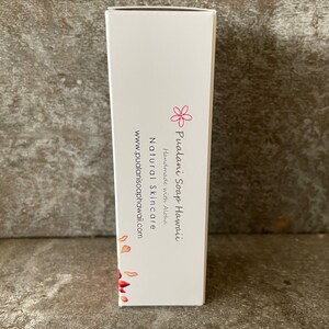May include: A white rectangular box with the text "Pualani Soap Hawaii" and "Natural Skincare" in black. A pink flower graphic and red petal design are also visible. The website address is www.pualanisoaphawaii.com.