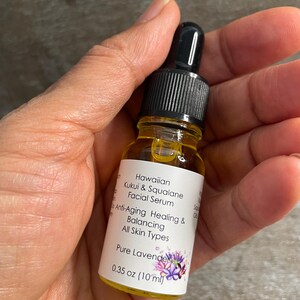 May include: A small glass bottle of Hawaiian Kukui & Squalane Facial Serum. The bottle has a black dropper top and a white label with text that reads "Anti-Aging Healing & Balancing All Skin Types". The bottle contains 10 ml of a clear, amber-coloured liquid.