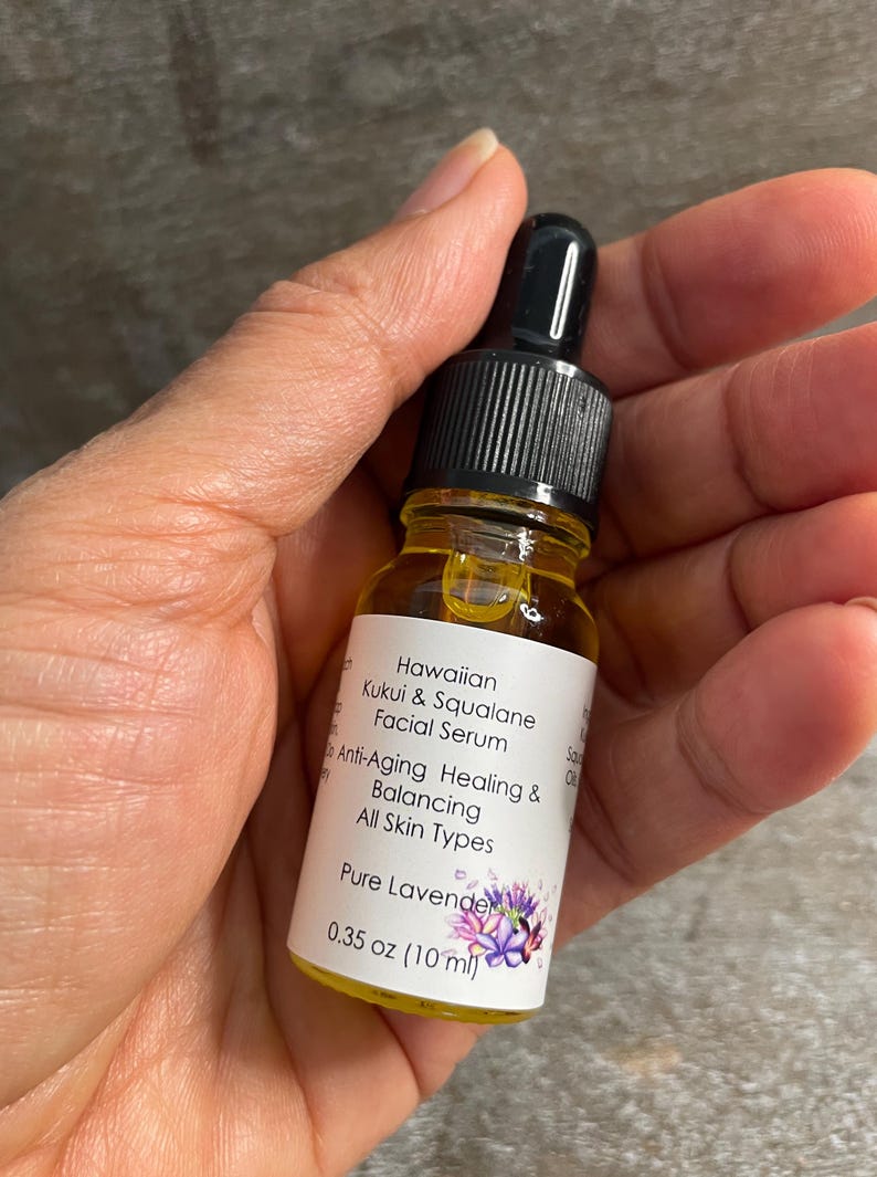 May include: A small glass bottle of Hawaiian Kukui & Squalane Facial Serum. The bottle has a black dropper top and a white label with text that reads "Anti-Aging Healing & Balancing All Skin Types". The bottle contains 10 ml of a clear, amber-coloured liquid.