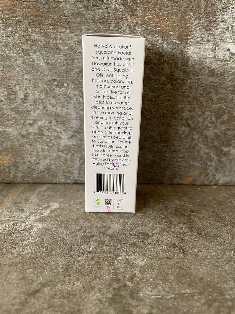 May include: A white product box detailing a facial serum made with Hawaiian Kukui Nut and Olive Squalane Oils. The text highlights anti-ageing, moisturising, and protective qualities for all skin types.