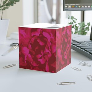 Può includere: Un porta blocchi notes quadrato in cartone con un motivo floreale rosa e rosso. Un blocco note bianco è posto sopra.