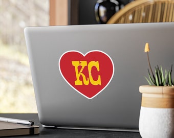 Adesivos de vinil recortados com as letras KC dentro de um coração