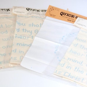 May include: Four Quick-Stitch cross-stitch kits in clear plastic packaging with paper headers. Each kit features light blue text on a cream-colored fabric background, with the phrase "Thou shalt love the Lord thy God with all thy heart".