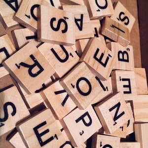 May include: A close-up of a pile of wooden letter tiles, commonly used in the game Scrabble. The tiles are arranged in a random order, with the letters facing up. The letters include A, S, R, O, E, N, B, U, I, and Y.