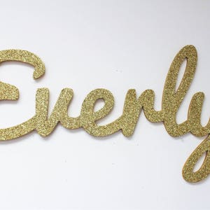 May include: Gold glitter letters spelling out the name "Everly".