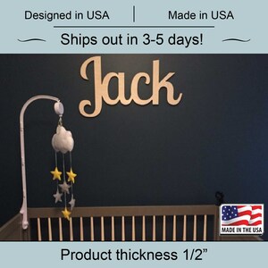May include: A wooden name sign with the name "Jack" in cursive script. The sign is mounted on a dark blue wall above a crib. The sign is 1/2 inch thick.