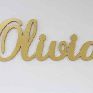 May include: Gold cursive script name sign with the name Olivia.