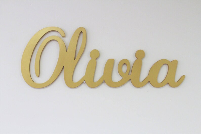 May include: Gold cursive script name sign with the name Olivia.