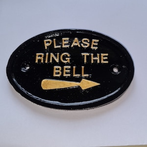 May include: Black oval sign with gold lettering that reads "Please ring the bell" with a gold arrow pointing to the right.