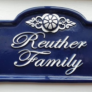 May include: A blue and white ceramic house number sign with the text "Reuther Family" in white cursive lettering.