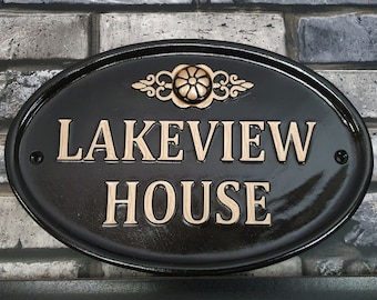 May include: Black oval house sign with gold lettering that reads "LAKEVIEW HOUSE". The sign has a decorative gold floral design at the top.
