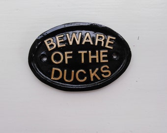 May include: Black oval sign with gold lettering that reads "BEWARE OF THE DUCKS".