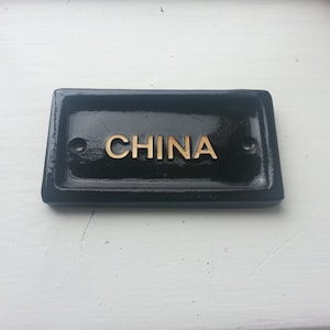 May include: Black rectangular sign with gold lettering that reads "CHINA".