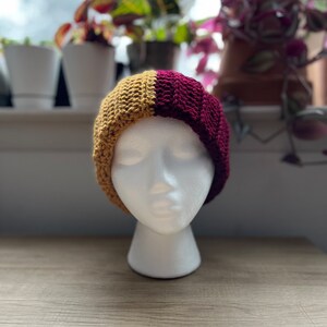 May include: A crocheted beanie hat with a split design. One half is a deep burgundy color and the other half is a mustard yellow color.