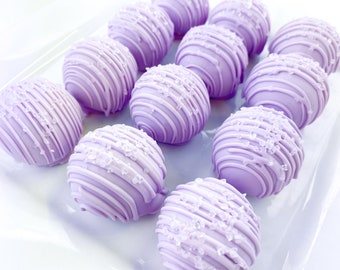 Puede incluir: Una fuente de cake pops cubiertos de chocolate morado decorados con rayas blancas y chispas.