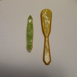 May include: Two vintage plastic shoe horns, one green and one yellow with a white swirl pattern.