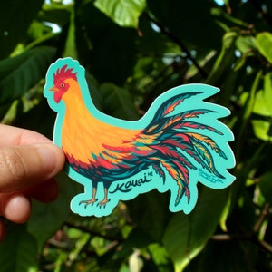 May include: A colorful sticker of a rooster with a long, flowing tail. The rooster is yellow, orange, red, and blue. The sticker is on a turquoise background and says "Kauai HI" in a white font.