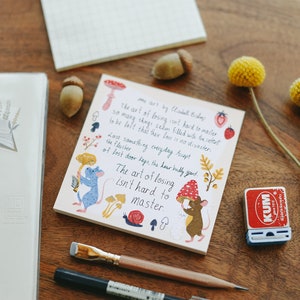 May include: A pink and white notebook with a hand-drawn illustration of a mouse holding a mushroom. The notebook features a quote from Elizabeth Bishop: "The art of losing isn't hard to master."