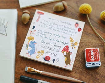May include: A pink and white notebook with a hand-drawn illustration of a mouse holding a mushroom. The notebook features a quote from Elizabeth Bishop: "The art of losing isn't hard to master."