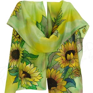 May include: A green silk scarf featuring a hand-painted design of sunflowers. The scarf is folded in half and the sunflowers are arranged in a cluster.
