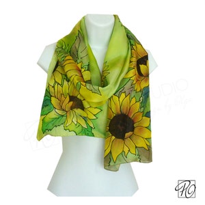 May include: A green silk scarf with a hand-painted design of sunflowers. The scarf is draped over a white mannequin.