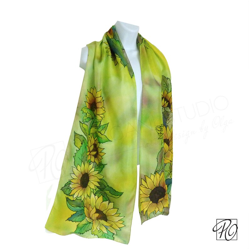 May include: A green silk scarf with a hand-painted design of sunflowers. The scarf is on a white background.