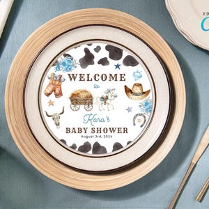 Puede incluir: Un plato de baby shower de vaca blanco y negro con detalles azules y marrones. El plato dice "Bienvenido al baby shower de Kara el 3 de agosto de 20XX".