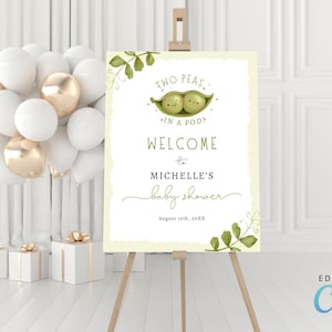 May include: A baby shower welcome sign on an easel. The sign features the text "Two Peas in a Pod" with a graphic of two peas in a pod. The sign also includes the text "Welcome to Michelle's baby shower".