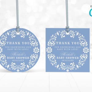 May include: Two baby shower tags, one round and one square, in a light blue color. Each tag has a white floral design around the edge and includes the text "Thank You" and "Baby Shower". The tags are connected to a gray string.