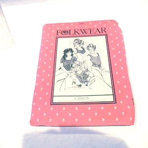 May include: A pink sewing pattern titled "FOLKWEAR" with a polka dot pattern. The pattern features a black and white illustration of four figures in vintage clothing. The word "CAMEOS" is printed below the illustration.