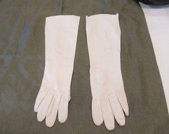 May include: A pair of white long gloves made of a soft, smooth fabric. The gloves are folded in half and laid flat on a green surface.