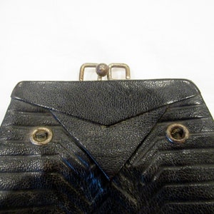 May include: Black vintage purse with a silver clasp. The purse has a textured, geometric design with horizontal lines and a triangular flap. Two metal eyelets are visible on the front.