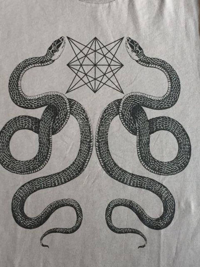 K&ouml;nnte beinhalten: Ein graues T-Shirt mit einem schwarz-wei&szlig;en grafischen Design aus zwei Schlangen, die sich um einen geometrischen Stern winden.